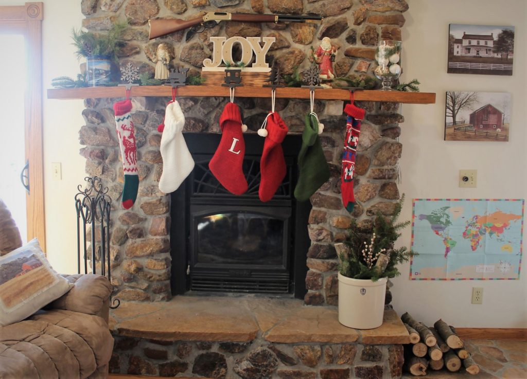 our fireplace decorated with pine bows, crock with pine bows, and a stack of wood logs